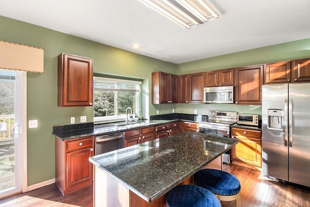 kitchen featuring sink, dark wood-type flooring, appliances with stainless steel finishes, dark stone countertops, and a center island