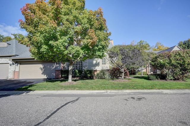 view of property hidden behind natural elements featuring a garage and a front lawn