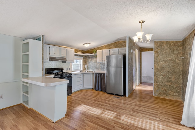 kitchen with lofted ceiling, decorative light fixtures, stainless steel refrigerator, black range with gas stovetop, and kitchen peninsula