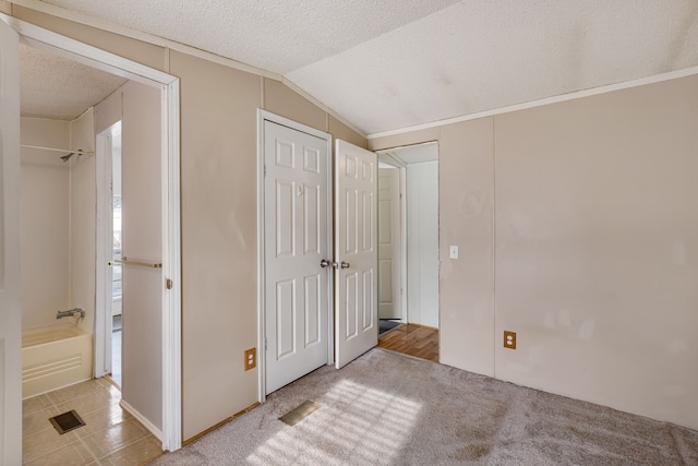 unfurnished bedroom with vaulted ceiling, light colored carpet, a textured ceiling, and a closet