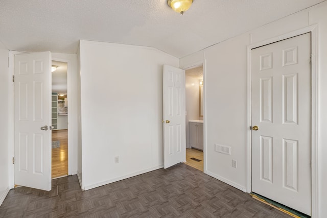 unfurnished bedroom with vaulted ceiling, a textured ceiling, and dark parquet floors