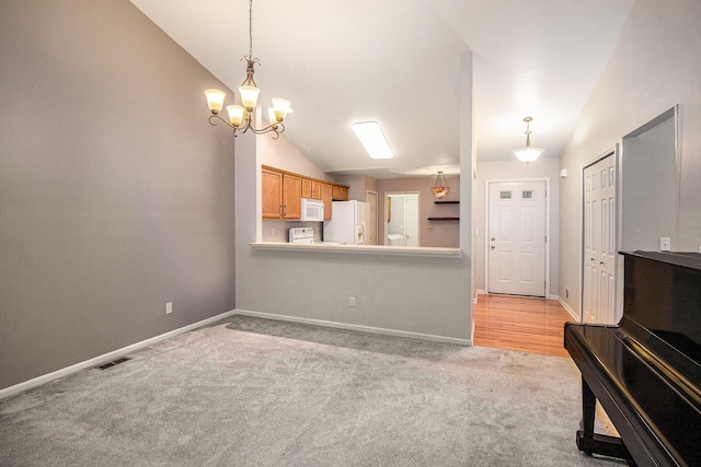 kitchen with hanging light fixtures, white appliances, vaulted ceiling, and light colored carpet