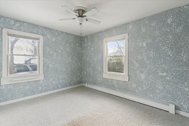 empty room with a baseboard radiator, carpet floors, and ceiling fan