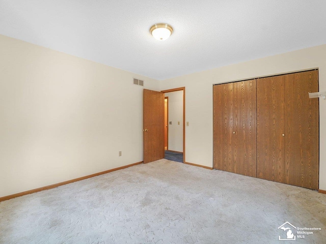 unfurnished bedroom with light colored carpet, a closet, and a textured ceiling