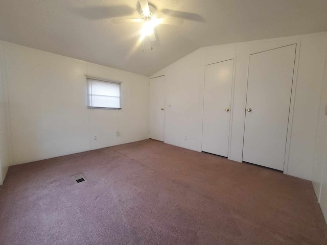 unfurnished bedroom with multiple closets, ceiling fan, carpet floors, and vaulted ceiling