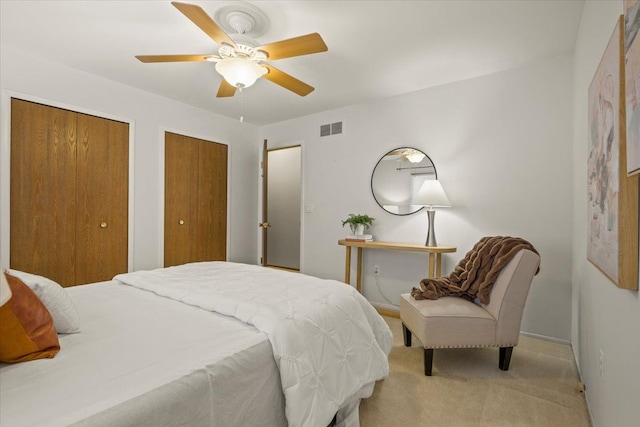 bedroom featuring two closets, light colored carpet, and ceiling fan