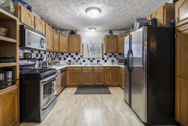 kitchen featuring sink, stainless steel appliances, light hardwood / wood-style floors, a textured ceiling, and decorative backsplash