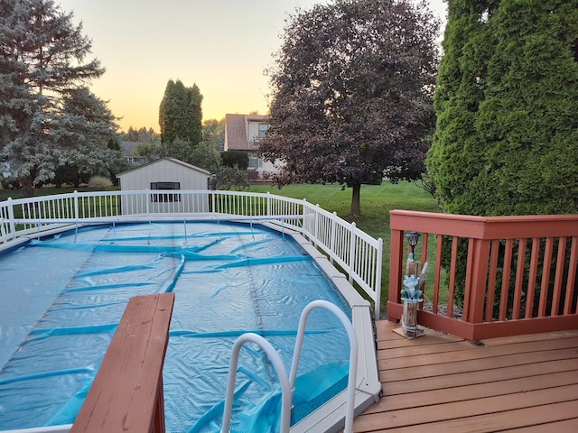 pool at dusk featuring a wooden deck, an outbuilding, and a yard