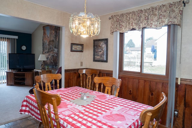 carpeted dining area featuring wooden walls and a notable chandelier