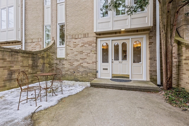 snow covered property entrance featuring a patio and brick siding