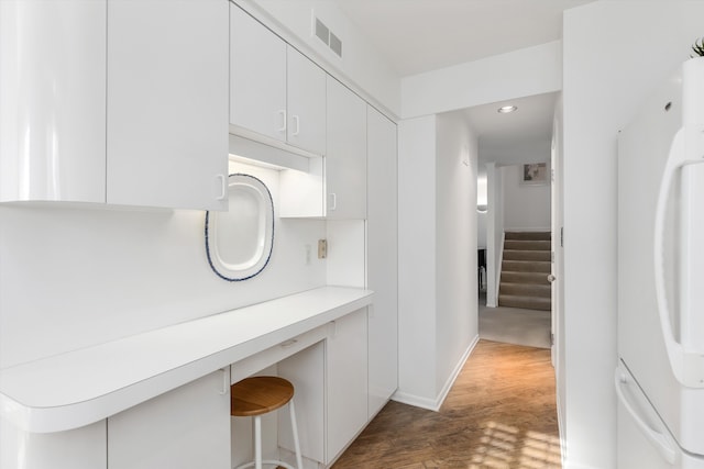 kitchen with white refrigerator, dark hardwood / wood-style floors, a breakfast bar, and white cabinets