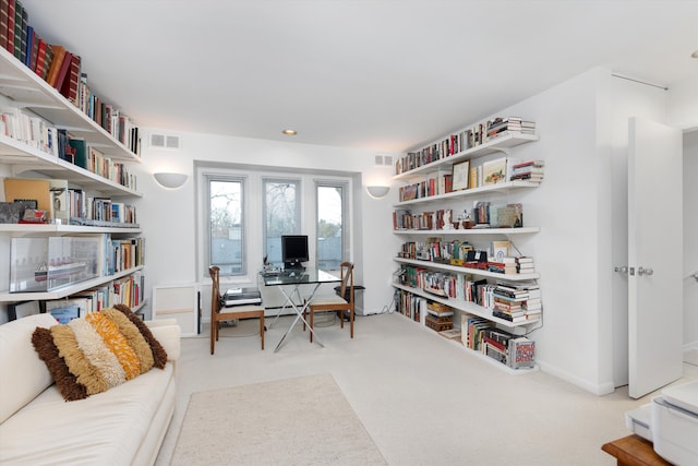 office area with carpet floors, wall of books, visible vents, and baseboards