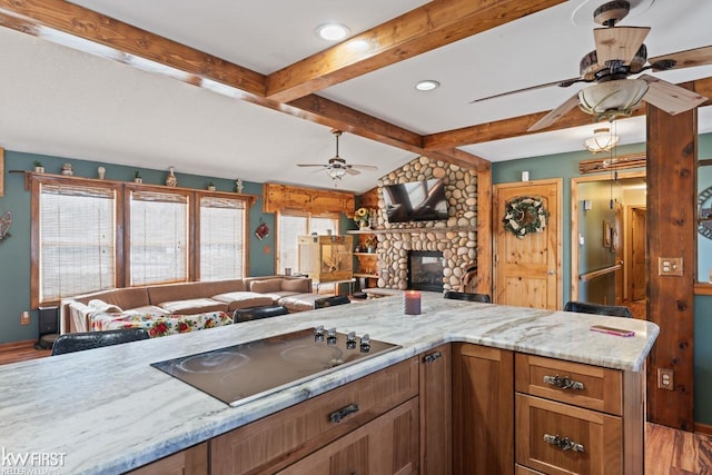 kitchen featuring ceiling fan, vaulted ceiling with beams, black electric stovetop, and light stone counters