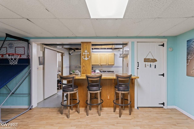 kitchen featuring a paneled ceiling, a kitchen breakfast bar, and light hardwood / wood-style floors