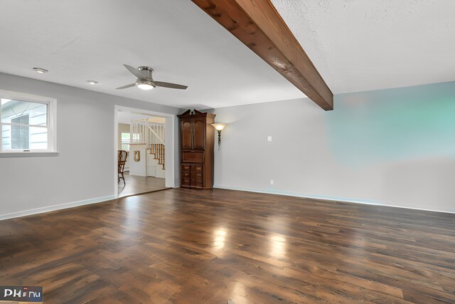 unfurnished living room with ceiling fan, dark wood-type flooring, and beamed ceiling