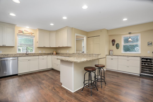 kitchen with sink, hanging light fixtures, stainless steel dishwasher, a kitchen breakfast bar, and beverage cooler