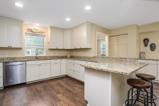 kitchen with dark wood-type flooring, sink, light stone counters, stainless steel dishwasher, and a kitchen breakfast bar