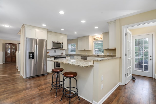 kitchen featuring a breakfast bar area, backsplash, stainless steel appliances, light stone countertops, and dark hardwood / wood-style flooring