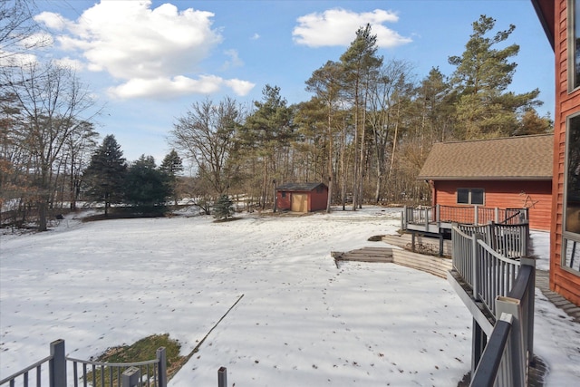 snowy yard with a storage shed and a deck