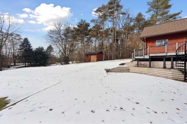 yard covered in snow featuring a wooden deck and a storage shed