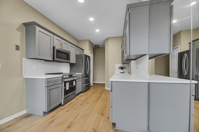 kitchen featuring backsplash, appliances with stainless steel finishes, kitchen peninsula, and gray cabinetry