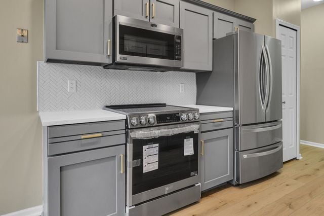 kitchen featuring gray cabinets, appliances with stainless steel finishes, light hardwood / wood-style flooring, and decorative backsplash