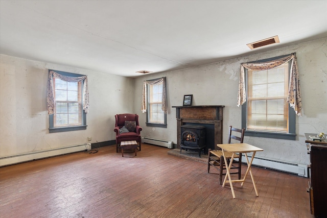 living area featuring hardwood / wood-style flooring, a wood stove, and a baseboard heating unit