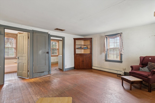 living area with dark hardwood / wood-style floors, a wealth of natural light, and a baseboard heating unit