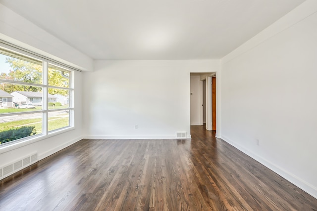 empty room with baseboards, visible vents, and dark wood finished floors