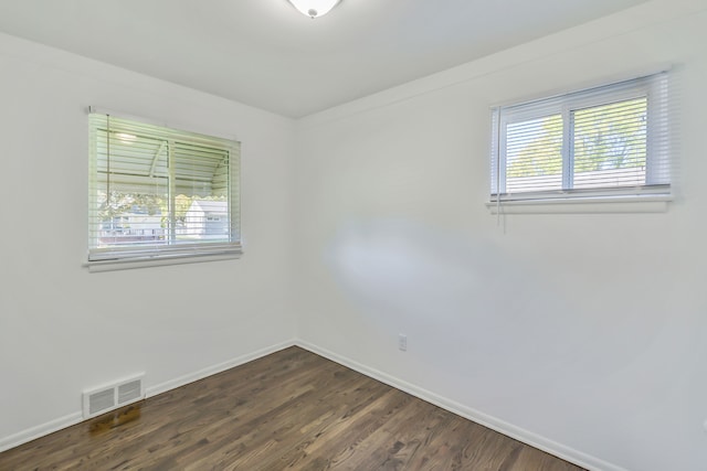 unfurnished room featuring dark wood-type flooring, visible vents, and baseboards