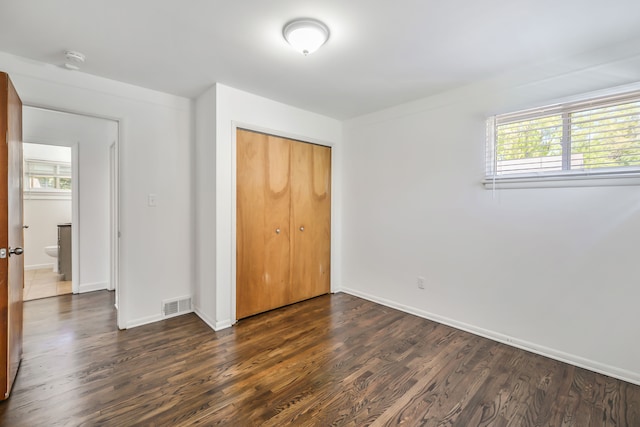 unfurnished bedroom with dark wood-type flooring, a closet, visible vents, and baseboards