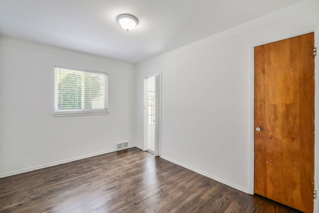 unfurnished room with dark wood-style flooring, visible vents, and baseboards