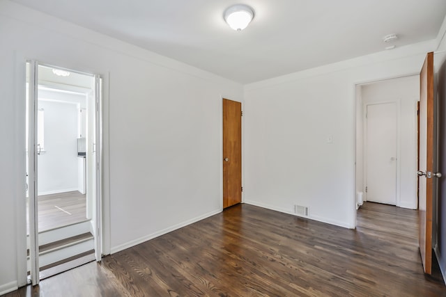 empty room featuring baseboards, visible vents, and dark wood finished floors