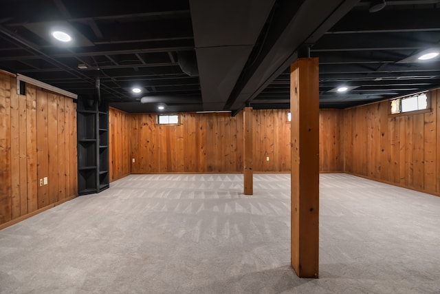 basement with light carpet, plenty of natural light, wooden walls, and baseboards