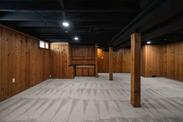 below grade area with light carpet, visible vents, and wooden walls