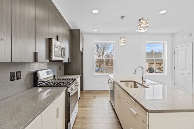 kitchen with sink, light stone counters, hanging light fixtures, appliances with stainless steel finishes, and an island with sink