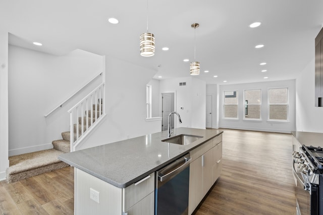 kitchen featuring pendant lighting, sink, appliances with stainless steel finishes, a kitchen island with sink, and light stone counters