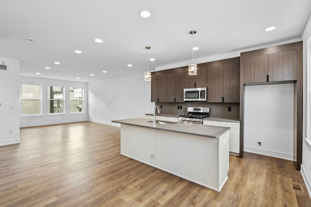 kitchen featuring sink, decorative light fixtures, light hardwood / wood-style flooring, appliances with stainless steel finishes, and a kitchen island with sink