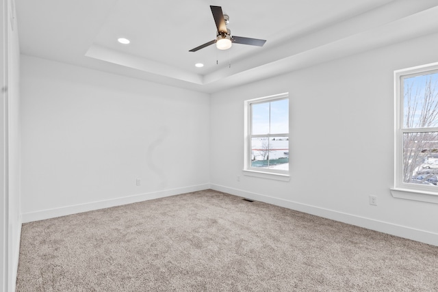 empty room with ceiling fan, a tray ceiling, and carpet floors