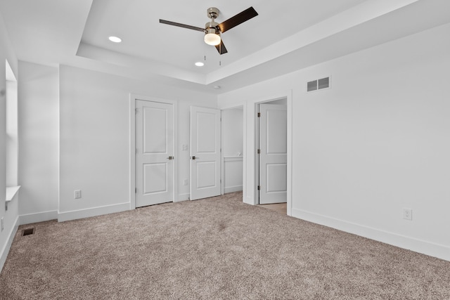 unfurnished bedroom featuring light colored carpet, a raised ceiling, and ceiling fan