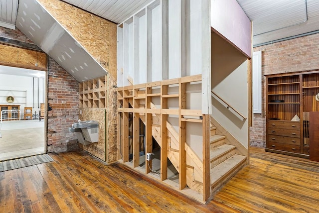 staircase featuring lofted ceiling, hardwood / wood-style flooring, and brick wall