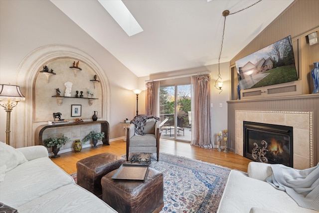 living room with high vaulted ceiling, a tile fireplace, wood-type flooring, and a skylight