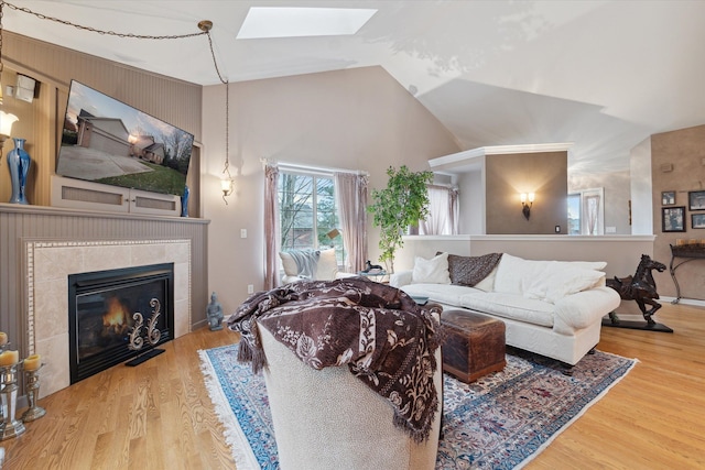 living room featuring a tiled fireplace, lofted ceiling with skylight, and hardwood / wood-style floors