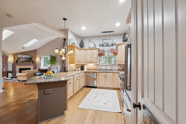 kitchen featuring light wood-type flooring, kitchen peninsula, decorative light fixtures, a tile fireplace, and dishwasher