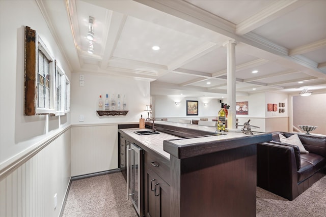 kitchen with coffered ceiling, light carpet, dark brown cabinets, a kitchen island with sink, and beam ceiling