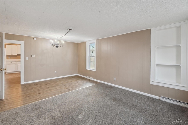 unfurnished room featuring an inviting chandelier, a textured ceiling, built in features, carpet, and a baseboard heating unit