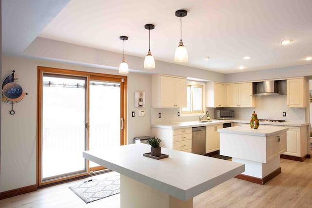 kitchen featuring pendant lighting, wall chimney range hood, light hardwood / wood-style flooring, stainless steel appliances, and a center island