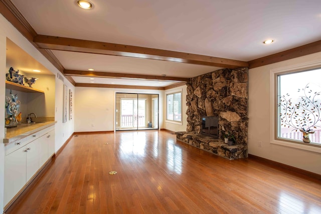 unfurnished living room with a stone fireplace, sink, crown molding, light wood-type flooring, and beam ceiling