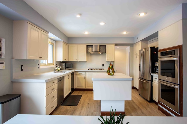 kitchen featuring sink, stainless steel appliances, a center island, light hardwood / wood-style floors, and wall chimney exhaust hood