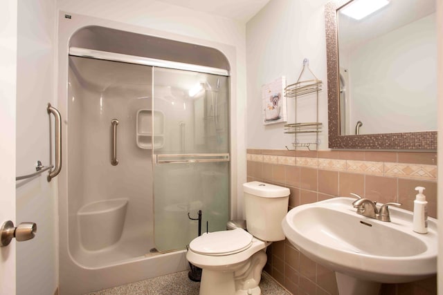 bathroom featuring toilet, a shower with shower door, sink, and tile walls